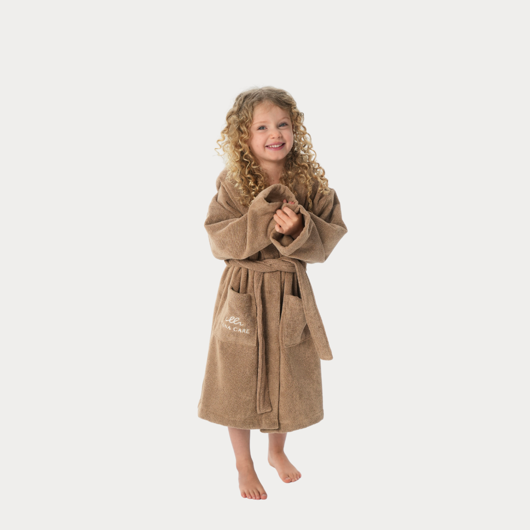Smiling child in a brown bathrobe with belt and pockets on a light background.